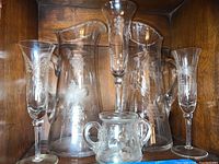 Photo showing two large and one medium etched crystal pitchers with grapevine patterns and three matching stemware glasses.