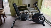 Side view of black and gray recumbent exercise bike showing the seat, backrest, pedals, and display console.