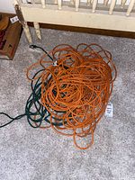 Orange and green industrial extension cords coiled on carpeted floor near radiator