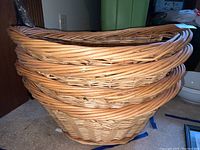 Stacked set of four natural wicker laundry baskets with woven handles and sturdy rims.