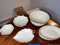Five white Lenox bowls with gold trim displayed on a wood table showing different shapes and sizes.