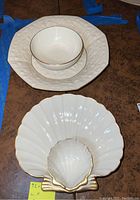 Photo showing an octagonal white Lenox dish with floral embossed pattern and gold trim, and a shell-shaped white dish with gold trim and small attached shell dip bowl.