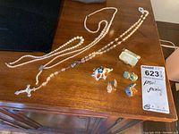 Three pearl necklaces laid out with several pairs of earrings, a decorative turtle figurine, and a brooch on a wooden surface.