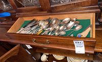 Drawer opened displaying assorted plated flatware including knives, forks, spoons, and serving pieces on a green felt liner.