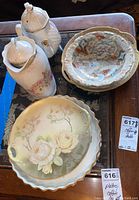 Various china platters and two teapots grouped together on a table, showing floral and textured decorations