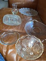 Overview of all six pressed glassware items arranged on surface showing plates, bowl, and vase with etched decorations.