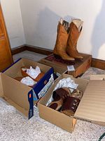 Two pairs of women's shoes in boxes on the floor, a pair of tan Larado boots on top of Larado boot box, and brown slip-on shoes inside a second box