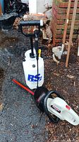 Photo showing the ReadySpray 2-gallon sprayer with black handle and hose along with the Craftsman 18-inch hedge trimmer lying on the ground.