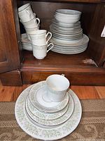 Photo showing stacked plates, bowls, cups and saucers inside cabinet and arranged outside.