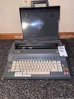 Open Smith Corona typewriter showing keyboard, ribbon area, and paper holder on carpeted floor