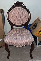 Front view of carved wooden chair with pink upholstered seat and backrest showing tufted fabric and curved legs.