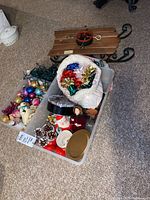 Overview of storage bin with assorted Christmas ornaments, bows, pinecones, string lights, bulbs, Santa figure, and doll along with wooden sled base.