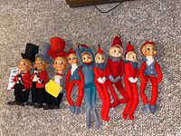 Nine vintage elf items displayed on carpet: three figurines with tall hats and six plush elf ornaments with fabric bodies and bells.