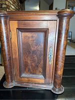 Front view of the wooden cabinet showing burled wood door panel and cylindrical side columns.