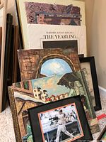 Various posters and art pieces leaning against a wall, showing multiple layers and edges of posters and frames in different sizes and colors.