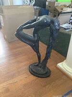 Image showing full view of the metal sculpture of a woman bending backward, hair flowing down to base, in indoor setting with boxes in background.