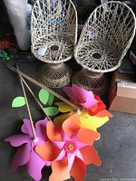 Two child-sized spun wicker chairs with pedestal bases displayed next to two colorful flower windmill stakes on the floor.