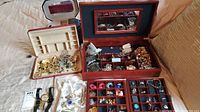 Photo showing two jewelry boxes filled with assorted costume jewelry including necklaces, bracelets, rings, earrings, dress pins, and hair combs scattered or organized in compartments.