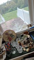 Wide view of figurines, glass bowls and a ceramic platter on a table by a window.
