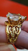 Close-up side profile showing ornate filigree band and prong-setting of the pear-shaped clear stone