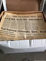 The Evening Sun newspaper in a cardboard box with headline 'Carter Elected President' plus other political news from the 1970s.