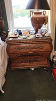 Front view of ornate carved wood nightstand with marble top and surface clutter