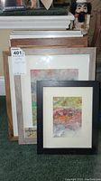 Stack of 13 framed paintings with visible variety in frame styles and sizes