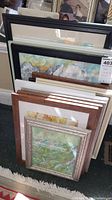 Photo showing a collection of 13 framed paintings of assorted sizes and frame styles, stacked vertically.