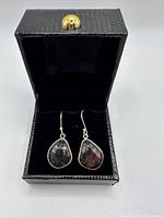 Pair of faceted brown sapphire earrings displayed inside a black jewelry box with textured exterior and gold-tone clasp.
