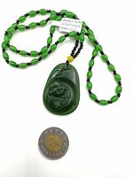 Full view of carved green jade Maitreya Buddha pendant on green and black bead necklace next to Canadian two-dollar coin for scale.