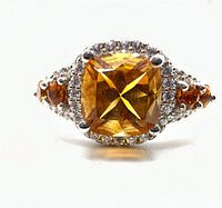 Front-facing view of ring showing cushion-cut orange center gemstone and clear halo