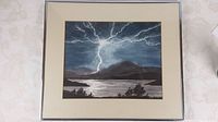 Full view of framed watercolour painting showing lightning strike over mountains and water.