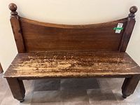 Front view of solid wood bench showing worn seat surface and high backrest with finials.