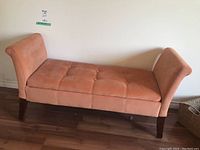 Front view of peach upholstered bench highlighting button tufted seat and upright padded ends
