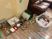 Wide view showing assortment of gift bags, wreath garland, boxes, and ornaments grouped near a couch on wood floor.