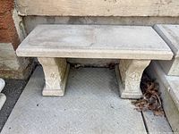 Front and top view of small rectangular concrete bench showing flat seat and two pedestal legs with floral designs.