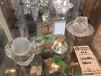 Photo of six decorative pieces including crystal and glass items arranged on a shelf with measurement tags from 3 to 5 inches.