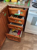 Four kitchen drawers partially open showing assortment of cutlery, utensils, and kitchen tools inside drawers.