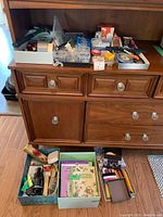 Wide view of wooden cabinet with upper trays and lower boxes containing assorted tools, hardware items, and office supplies.