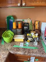 Kitchen counter with kitchenware items including strainers, Tupperware containers, grater, oil bottle, egg coddlers, salt and pepper shakers, and cutting boards
