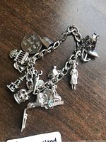 Full view of the sterling silver charm bracelet laid flat showing all attached charms including Gemini zodiac sign, crown, thimble, shoe, anchor, and figurine.