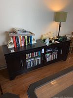 Front view of dark wood TV stand showing glass-front cabinet doors, enclosed side storage, and items on top.