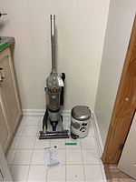 Full view of Hoover Air Sprint upright vacuum cleaner with attached cleaning head, manual on floor, and small metal garbage bin with lid at side.