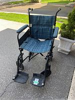Front view of the Airgo wheelchair showing tartan fabric upholstery on seat and backrest, padded armrests, footrests, and front wheels.