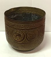 Front view of antique brass planter showcasing hand-tooled ornate circular medallion designs with elephants and floral motifs.