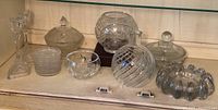 Full view of the crystal and glassware collection including decanter, bowls with lids, candlesticks, and coasters arranged on a shelf.