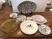 View of all plates and dishes displayed on wood table, showing variety and patterns including amber depression glass pieces and floral chintz plates.