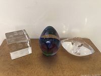 Photo of three paperweights including a dice, colored egg shape, and leaf design