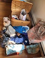 Lot of knitting supplies showing basket, bags, yarn skeins and unfinished knit projects.