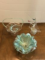 Three art glass pieces: Murano bowl, handled dish, and glass ship on wooden surface.